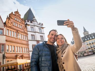 Ansicht auf ein Paar, welches beim Flanieren über den Hauptmarkt in Trier gerade ein Selfie macht. 
