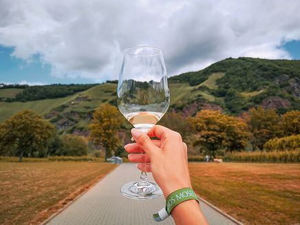 Mythos Mosel © Elina Leitz Ansicht auf ein Weinglas mit Moselpanorama. Die Frau, die das Weinglas in der Hand hält trägt ein Eintrittsband von Mythos Mosel.