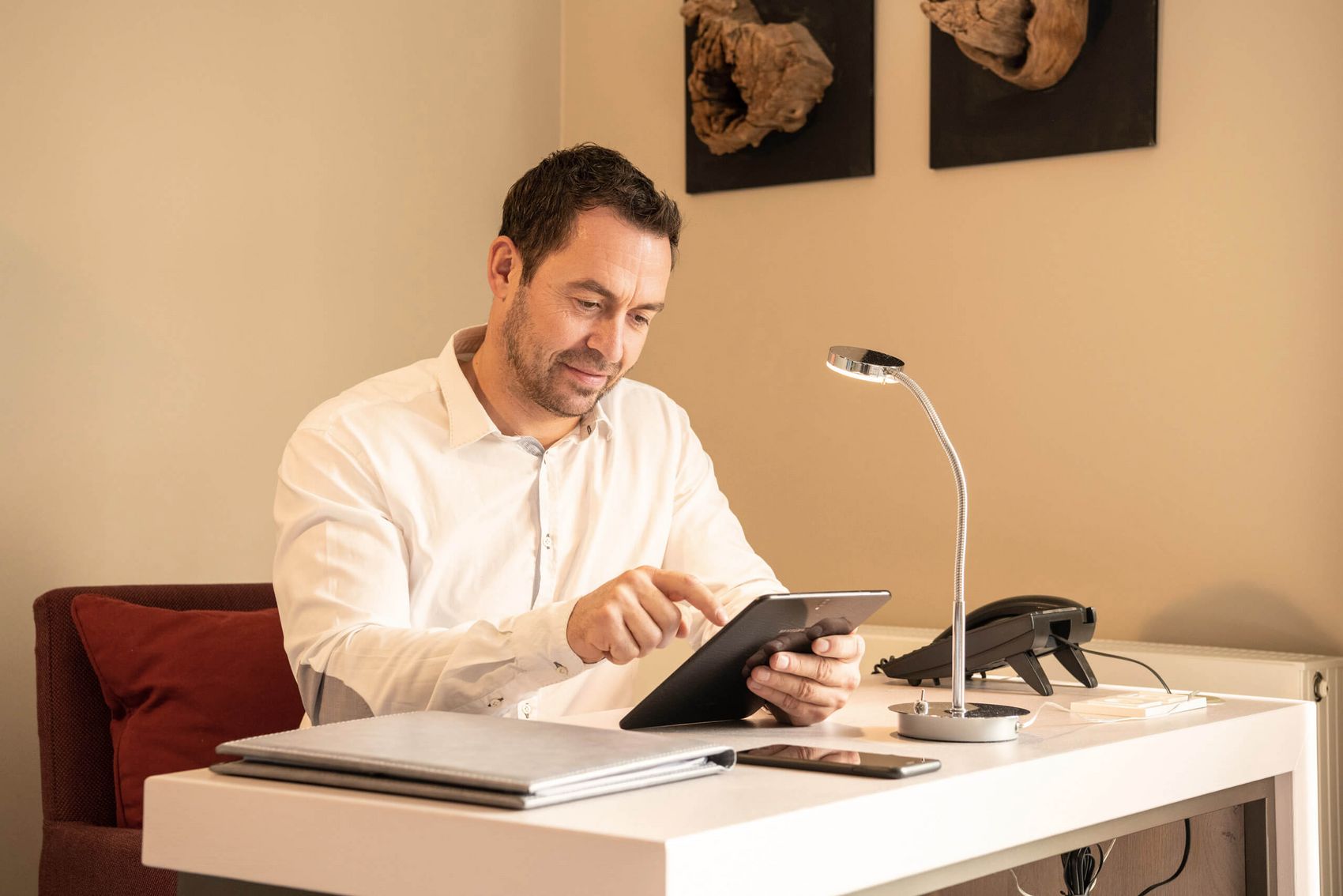 Workation: Arbeit und Urlaub verbinden © D. Ketz / MLT GmbH Mann sitzt an Schriebtisch in Hotelzimmermit Tablet