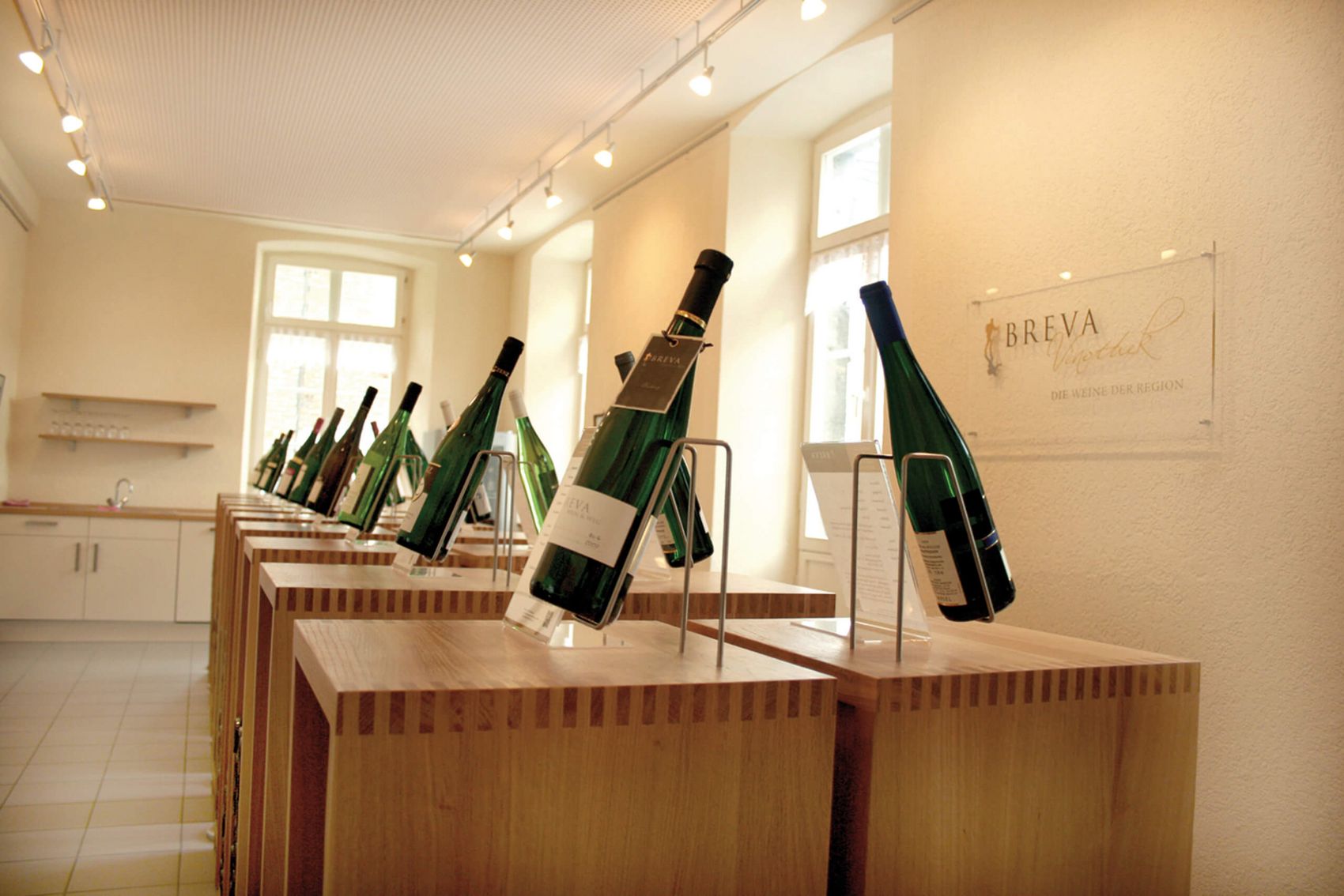 Ernst, Verkostungsraum der Vinothek Breva © BREVA Wein & Weg e.V. Weinflaschen auf Holzaufstellern präsentiert in hellem Raum